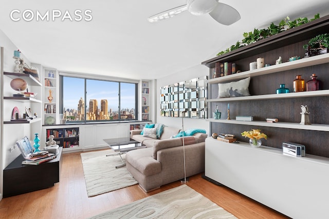 living area with a view of city, wood finished floors, and a ceiling fan