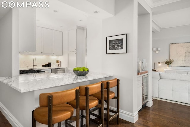 kitchen with stainless steel dishwasher, kitchen peninsula, light stone countertops, a breakfast bar area, and white cabinets