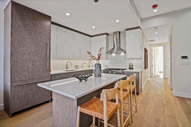 kitchen featuring a kitchen island, a kitchen bar, sink, white cabinets, and wall chimney exhaust hood