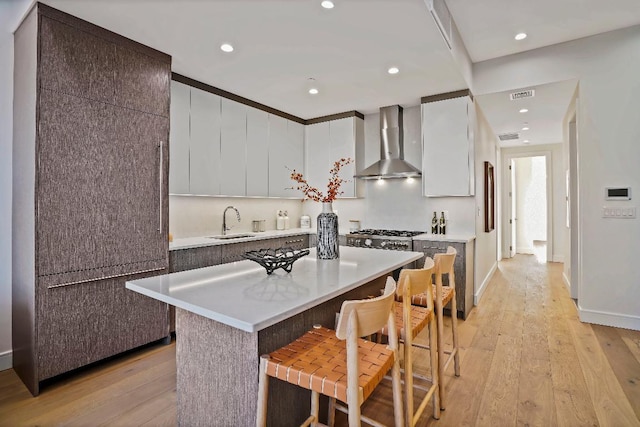 kitchen featuring a center island, a kitchen bar, sink, white cabinetry, and wall chimney exhaust hood