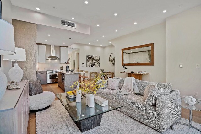 kitchen featuring white cabinetry, stainless steel range, a breakfast bar area, a kitchen island with sink, and wall chimney exhaust hood