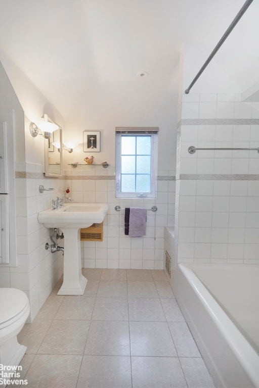 bathroom featuring tile patterned floors, toilet, tiled shower / bath combo, and tile walls