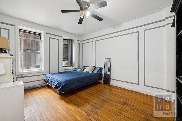 bedroom featuring wood-type flooring, a decorative wall, and ceiling fan