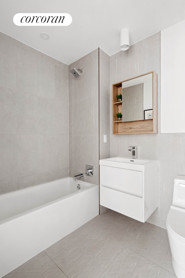 bathroom with toilet, tile patterned floors,  shower combination, vanity, and tile walls