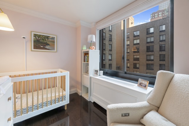 bedroom with dark wood-type flooring, a crib, and ornamental molding