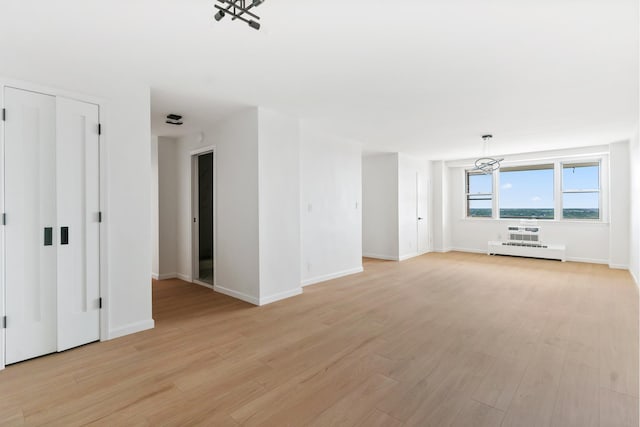 unfurnished living room with light wood-type flooring, a baseboard radiator, a chandelier, and baseboards