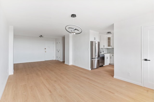 unfurnished living room with a chandelier, light wood-style floors, baseboards, and a sink