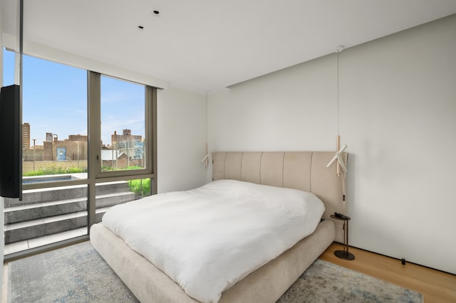 bedroom with expansive windows, wood finished floors, and a city view