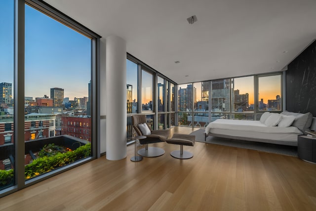 bedroom with expansive windows, a city view, multiple windows, and wood finished floors