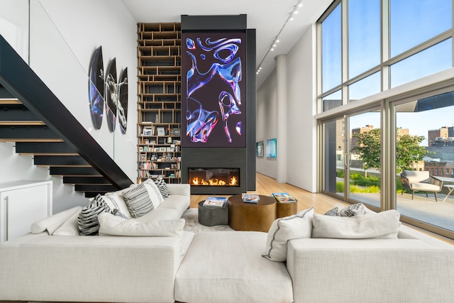 living room with a towering ceiling, a large fireplace, wood finished floors, and rail lighting