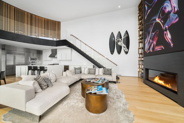 living area featuring a large fireplace, a high ceiling, stairway, and light wood-type flooring