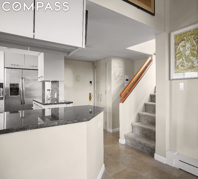 kitchen featuring stainless steel refrigerator with ice dispenser, a baseboard heating unit, dark stone countertops, and white cabinets