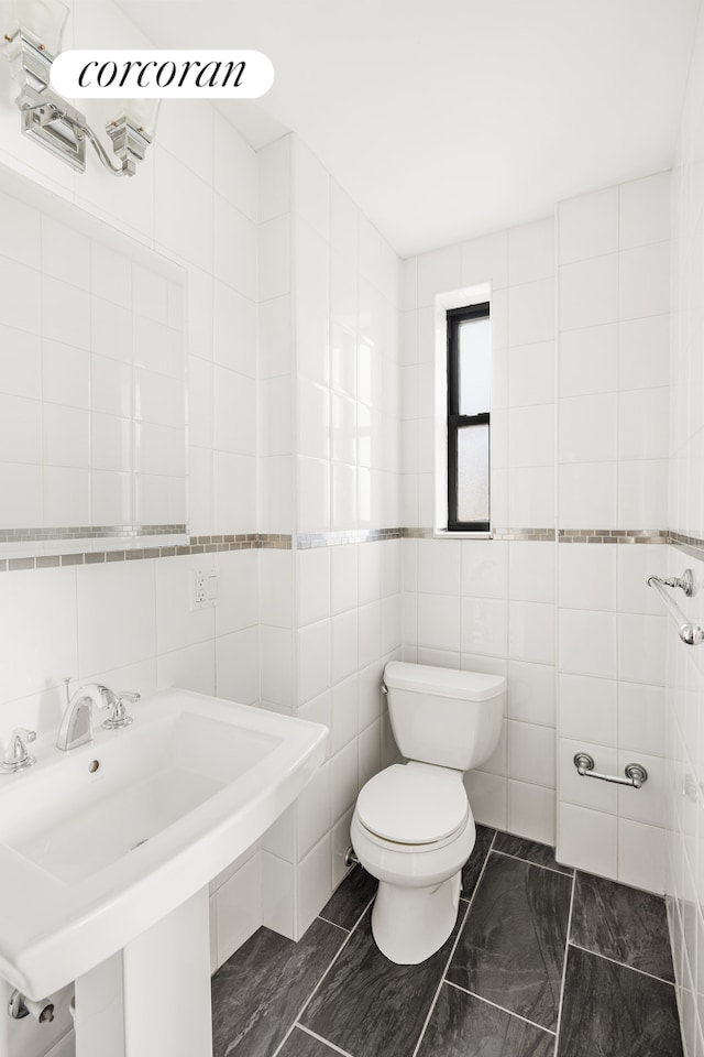 bathroom featuring a sink, tile walls, and toilet