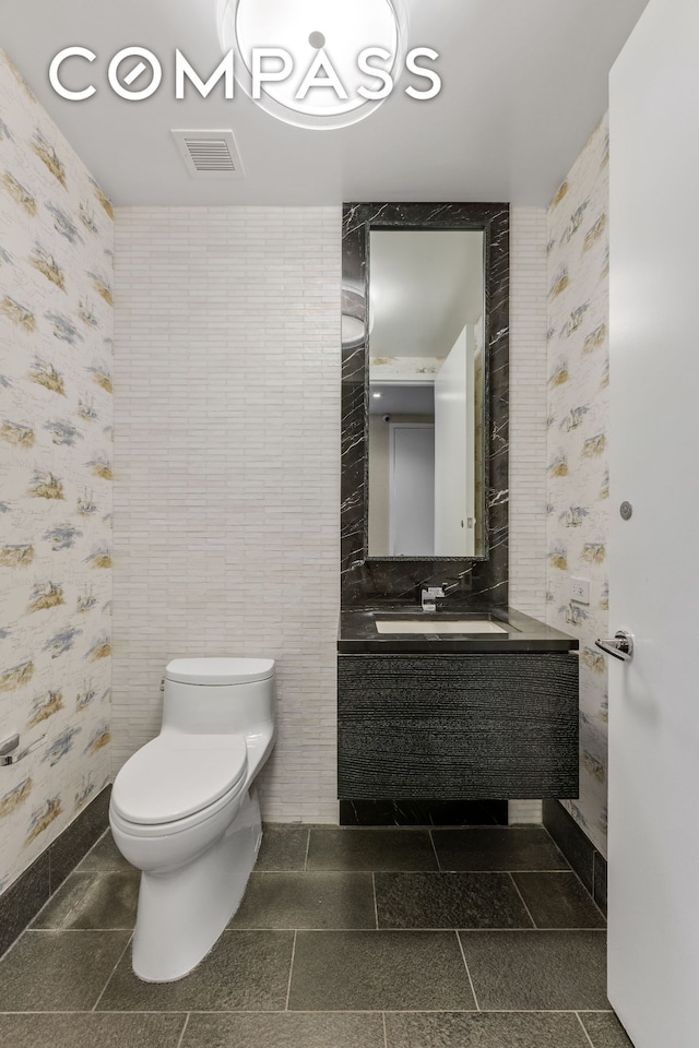 half bath with wallpapered walls, toilet, vanity, and baseboards