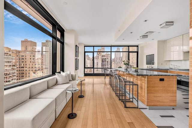 interior space featuring a kitchen bar, sink, light hardwood / wood-style flooring, wall oven, and white cabinets