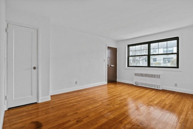 unfurnished room featuring radiator, light wood finished floors, and baseboards