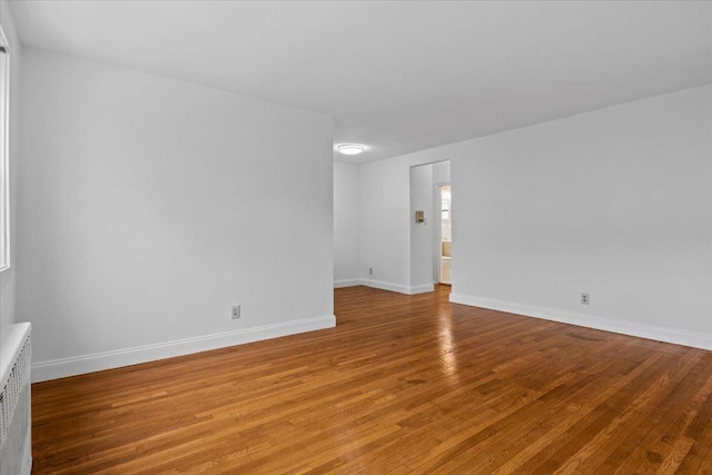 empty room featuring light wood finished floors, baseboards, and radiator