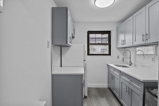 kitchen featuring a sink, light countertops, gray cabinets, light wood finished floors, and tasteful backsplash