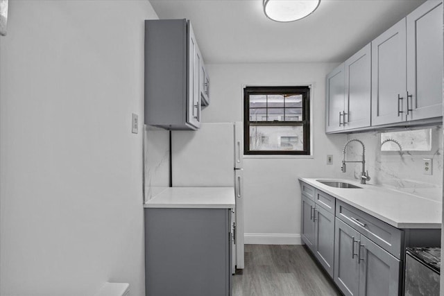 kitchen featuring baseboards, a sink, light countertops, light wood-type flooring, and gray cabinets