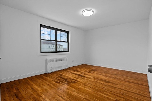 empty room with radiator heating unit, baseboards, and wood finished floors