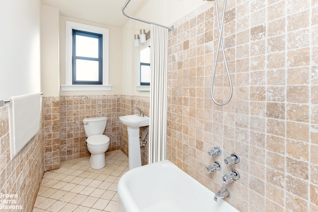 full bathroom featuring toilet, a wainscoted wall, tile patterned floors, washtub / shower combination, and tile walls