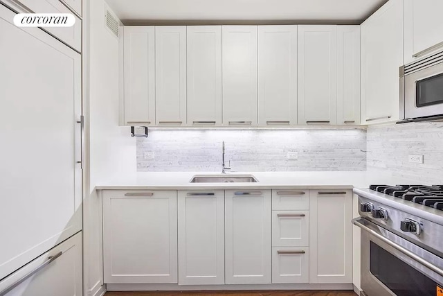 kitchen with stainless steel appliances, light countertops, backsplash, white cabinets, and a sink