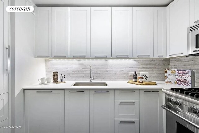 kitchen with white cabinets, appliances with stainless steel finishes, a sink, light countertops, and backsplash