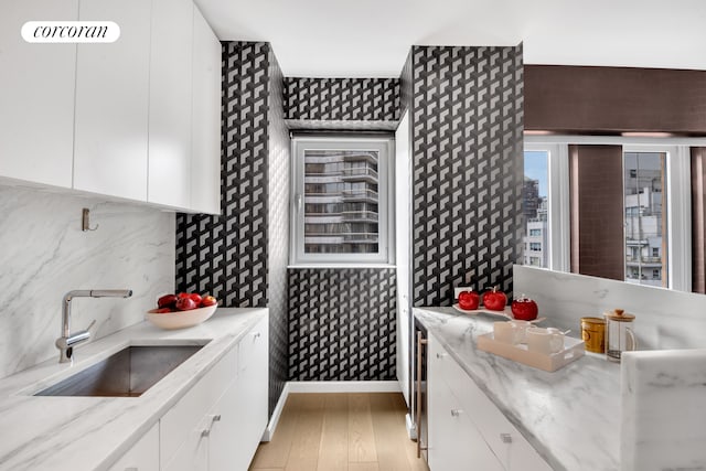 kitchen featuring light wood finished floors, decorative backsplash, white cabinetry, a sink, and baseboards