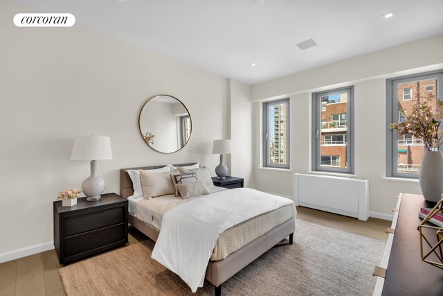 bedroom with radiator heating unit, wood finished floors, visible vents, and baseboards