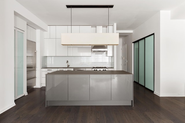 kitchen featuring white cabinets, wall chimney range hood, backsplash, dark wood-style flooring, and modern cabinets