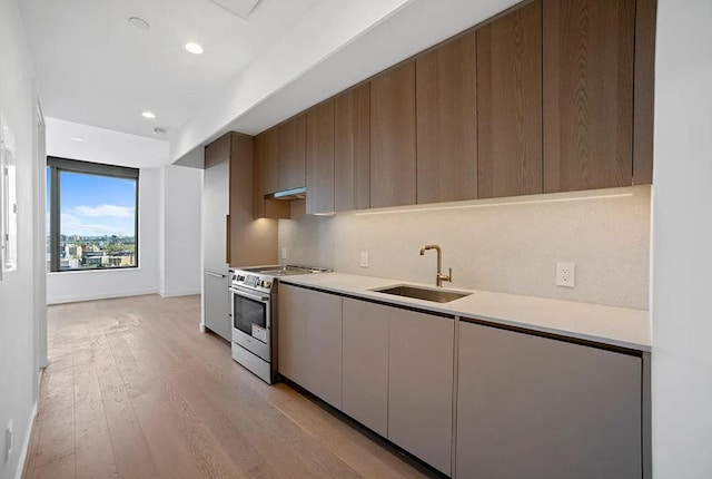 kitchen featuring stainless steel electric stove, sink, tasteful backsplash, and light wood-type flooring