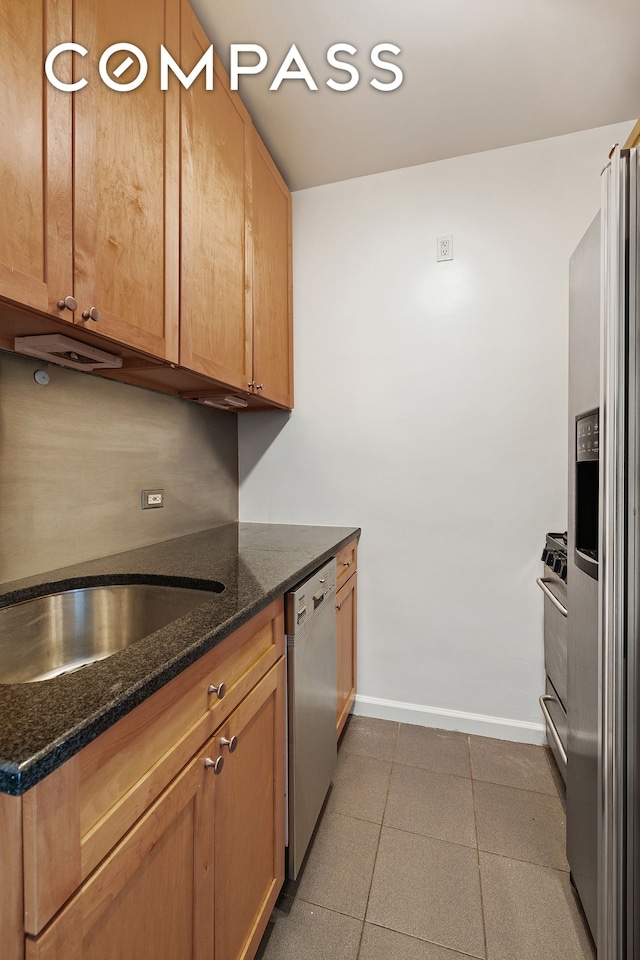 kitchen with appliances with stainless steel finishes, a sink, dark stone countertops, baseboards, and tile patterned floors