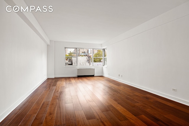 empty room with dark wood-style flooring, baseboards, and radiator heating unit