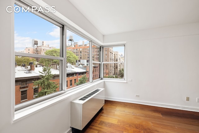 spare room with radiator heating unit, a view of city, baseboards, and wood finished floors