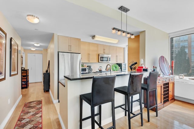 kitchen with light brown cabinets, stainless steel appliances, dark countertops, a kitchen bar, and pendant lighting