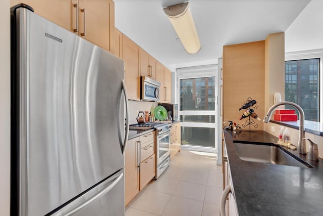 kitchen featuring stainless steel appliances, light brown cabinetry, dark countertops, and a sink