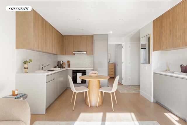 kitchen with black stovetop, sink, oven, decorative backsplash, and light hardwood / wood-style floors