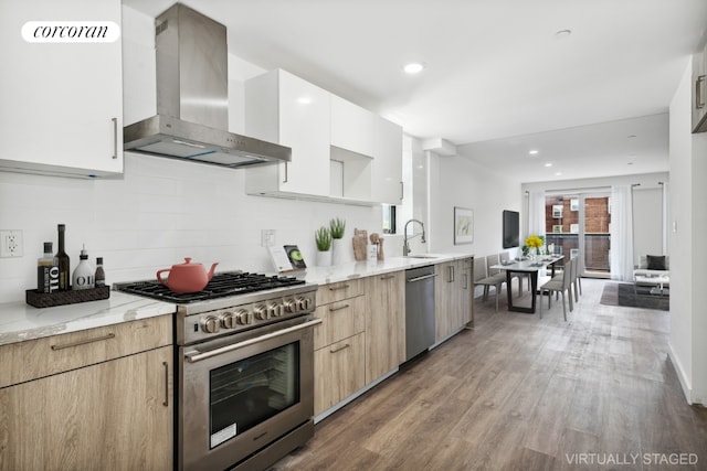 kitchen with sink, hardwood / wood-style flooring, light stone countertops, appliances with stainless steel finishes, and wall chimney exhaust hood