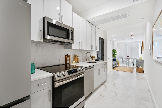 kitchen featuring marble finish floor, stainless steel appliances, decorative backsplash, white cabinets, and a sink