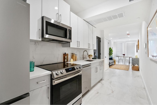 kitchen featuring decorative backsplash, white cabinets, appliances with stainless steel finishes, and sink