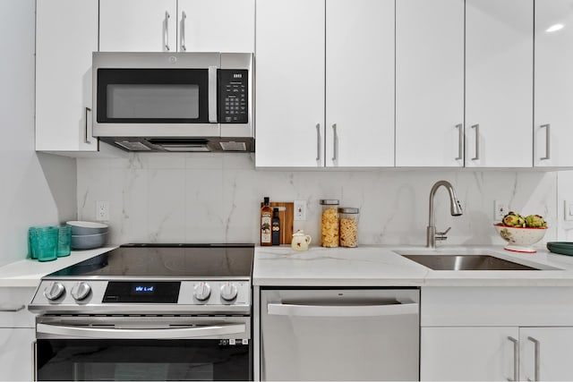 kitchen featuring tasteful backsplash, appliances with stainless steel finishes, white cabinets, a sink, and light stone countertops