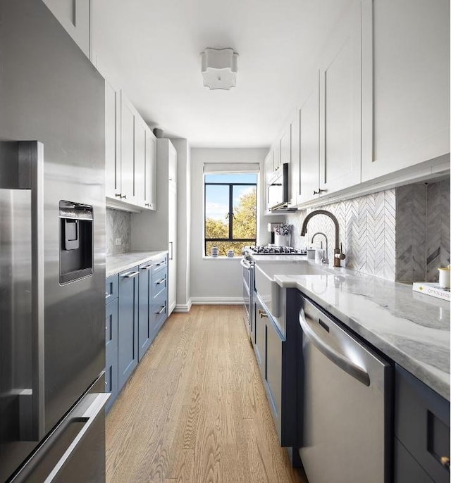 kitchen with white cabinetry, light stone counters, light hardwood / wood-style flooring, stainless steel appliances, and backsplash