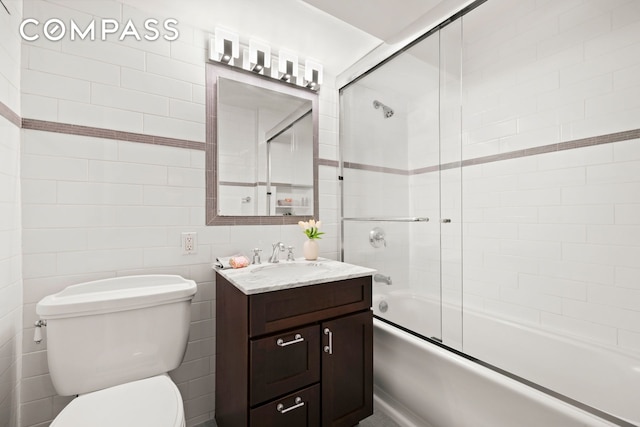 bathroom with toilet, vanity, tile walls, and bath / shower combo with glass door