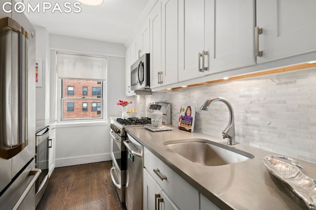 kitchen featuring dark wood-type flooring, a sink, backsplash, appliances with stainless steel finishes, and white cabinets