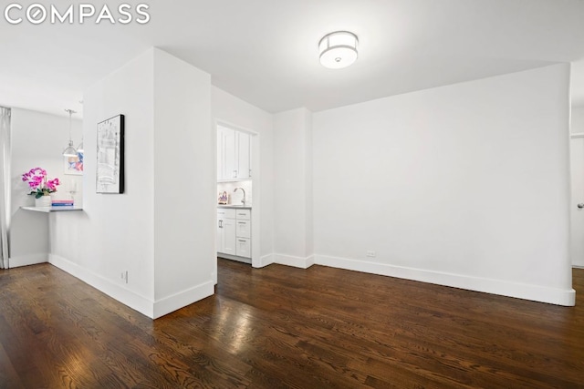 unfurnished room with a sink, baseboards, and dark wood finished floors