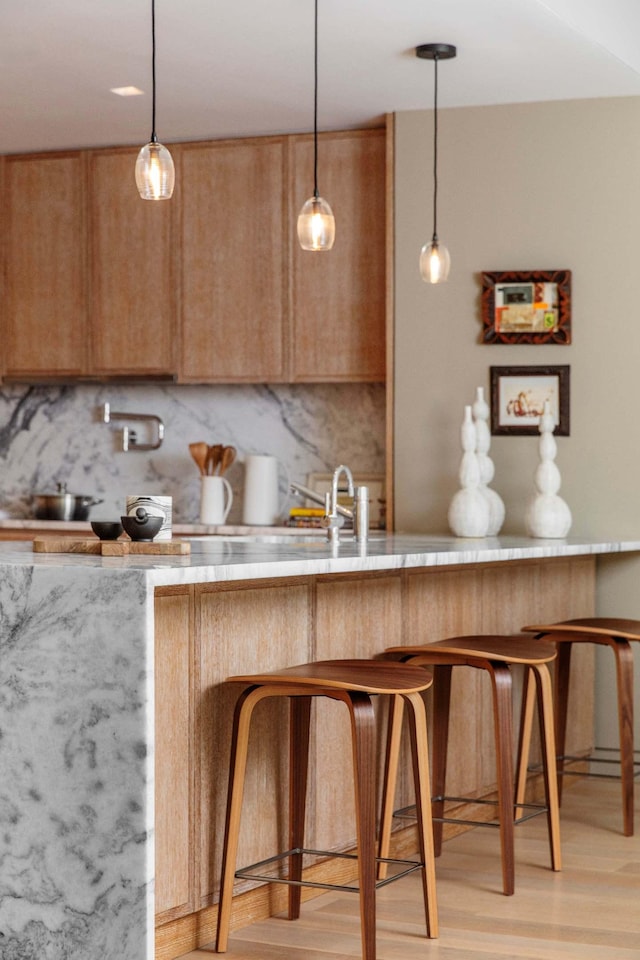 kitchen featuring decorative light fixtures, backsplash, a breakfast bar, and light wood-style flooring