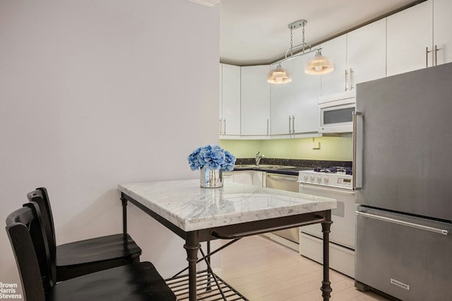 kitchen with pendant lighting, white cabinetry, sink, light hardwood / wood-style floors, and stainless steel appliances