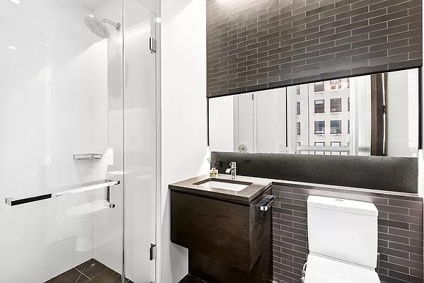 bathroom featuring a shower with shower door, vanity, toilet, and brick wall