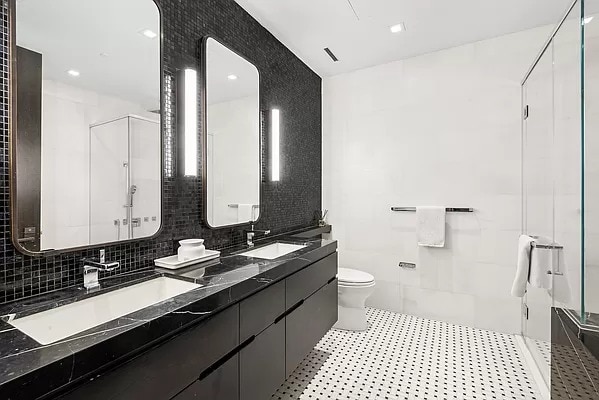 bathroom featuring toilet, double vanity, a sink, and a shower with shower door