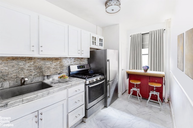 kitchen with sink, white cabinets, backsplash, light stone counters, and stainless steel appliances